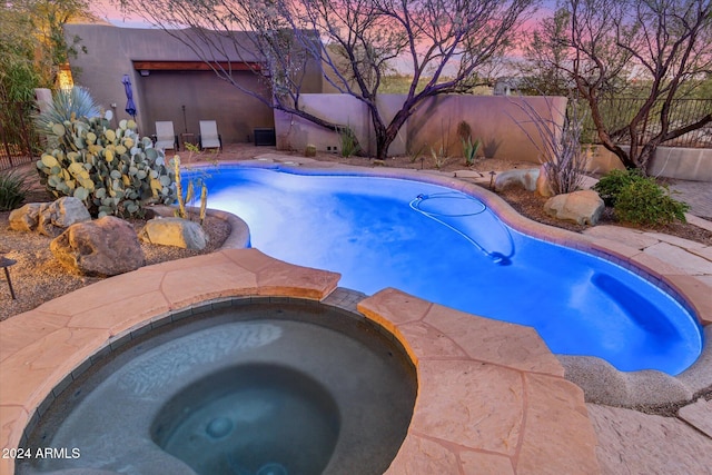 pool at dusk featuring an in ground hot tub