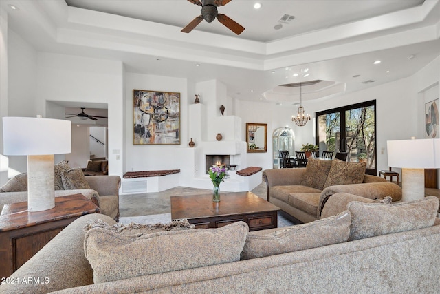 living room with ceiling fan with notable chandelier, a large fireplace, and a raised ceiling