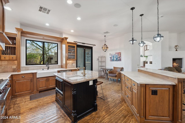 kitchen with light stone countertops, dark hardwood / wood-style flooring, sink, decorative light fixtures, and an island with sink