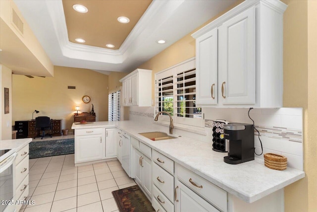 kitchen featuring kitchen peninsula, sink, white cabinets, backsplash, and a tray ceiling