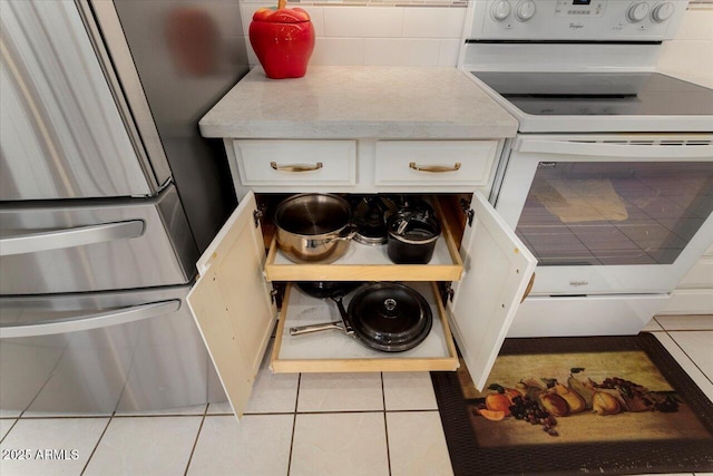 kitchen with electric stove, light tile patterned flooring, tasteful backsplash, and white cabinets