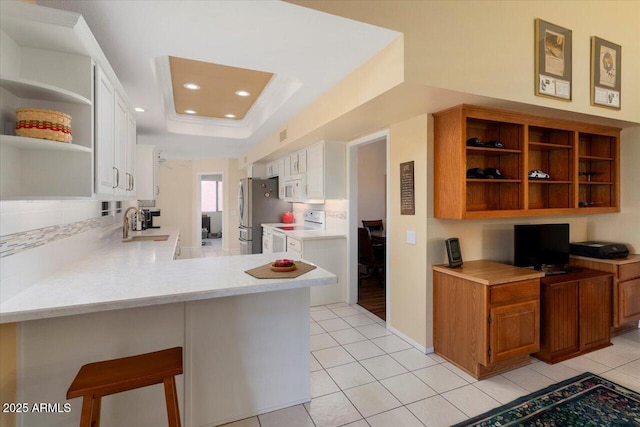 kitchen with light tile patterned flooring, white cabinetry, kitchen peninsula, a raised ceiling, and white appliances