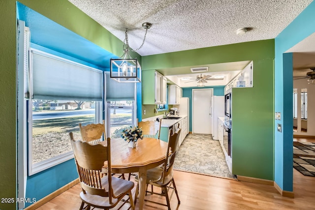 dining space featuring a textured ceiling, ceiling fan with notable chandelier, light hardwood / wood-style flooring, and sink