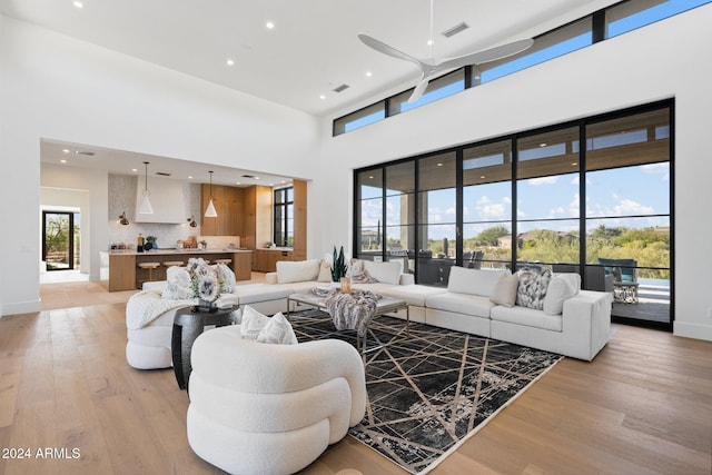 living room with ceiling fan, a high ceiling, and light hardwood / wood-style flooring