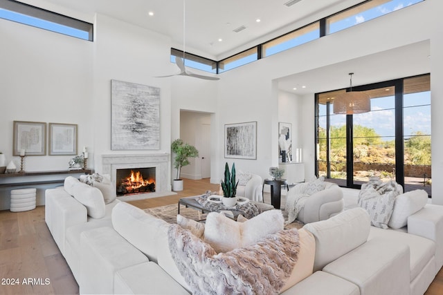 living room featuring a large fireplace, ceiling fan, light hardwood / wood-style floors, and a high ceiling