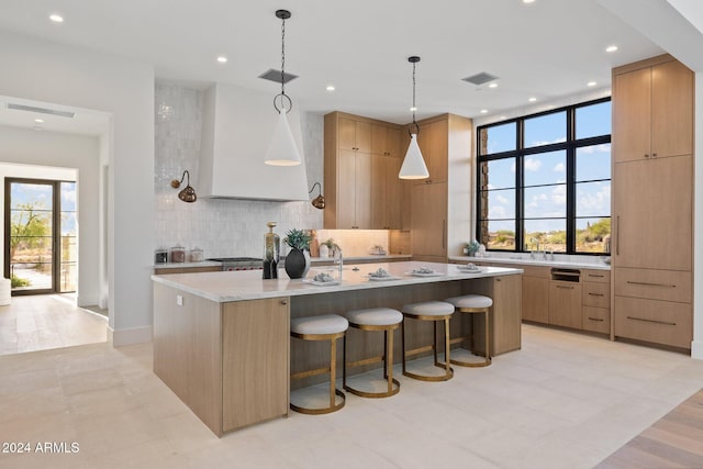 kitchen with backsplash, light stone counters, a breakfast bar, a kitchen island with sink, and pendant lighting