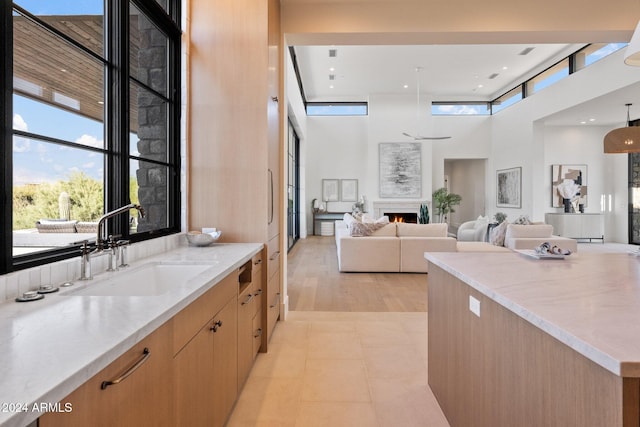 kitchen with a towering ceiling, light stone counters, sink, light brown cabinets, and light hardwood / wood-style flooring