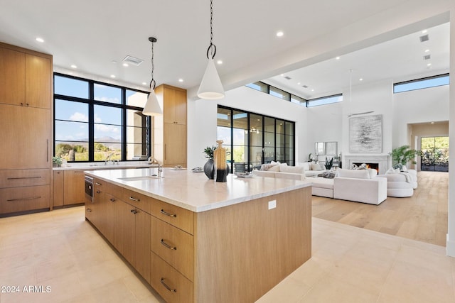 kitchen with light stone countertops, a towering ceiling, a spacious island, sink, and decorative light fixtures