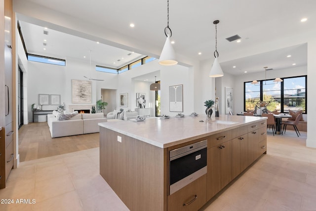 kitchen with a high ceiling, sink, decorative light fixtures, light wood-type flooring, and a large island