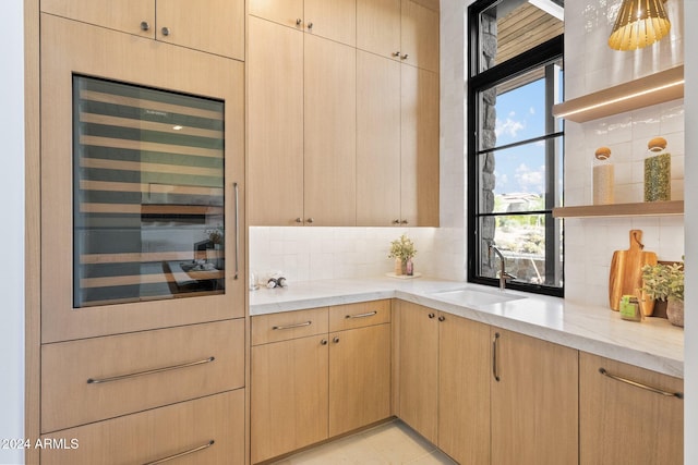 kitchen featuring tasteful backsplash, light stone countertops, light brown cabinetry, and sink