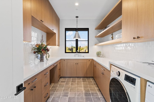 kitchen featuring washer and clothes dryer, backsplash, sink, hanging light fixtures, and light tile patterned floors