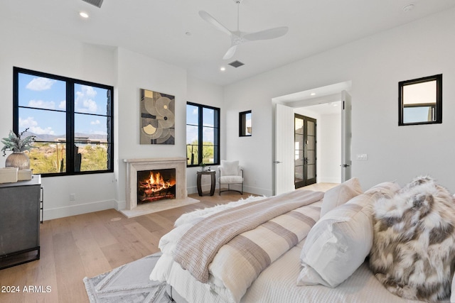 bedroom featuring ceiling fan, light hardwood / wood-style flooring, a high end fireplace, and french doors