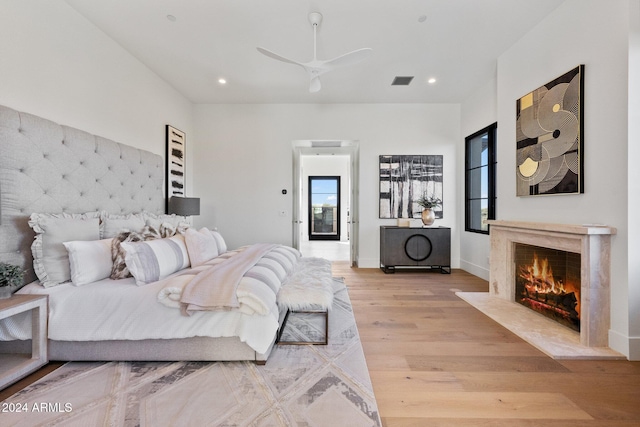 bedroom with a fireplace, light hardwood / wood-style floors, and ceiling fan