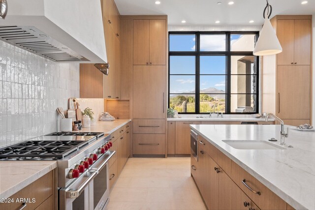 kitchen with light stone countertops, wall chimney exhaust hood, designer range, sink, and hanging light fixtures