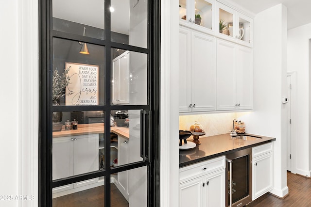 bar featuring beverage cooler, dark wood finished floors, backsplash, and a sink