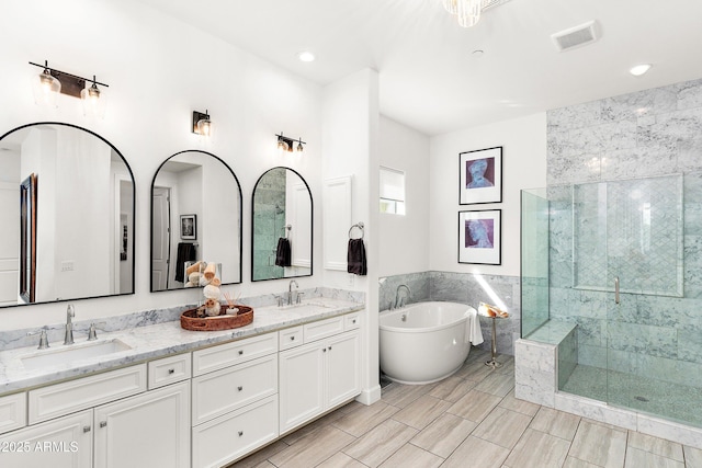 full bathroom with double vanity, a freestanding tub, a shower stall, and a sink