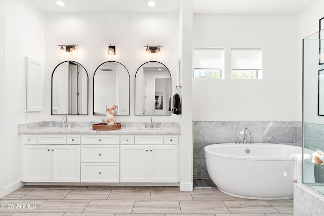 bathroom featuring wood tiled floor, a freestanding tub, a sink, and double vanity