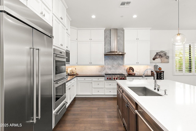 kitchen with built in appliances, a sink, visible vents, a warming drawer, and wall chimney exhaust hood