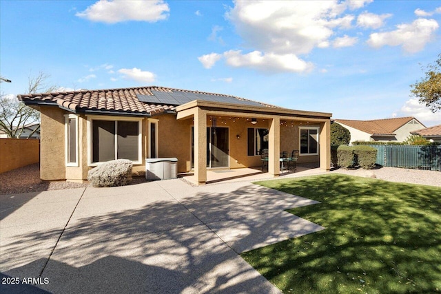 rear view of property featuring a patio, a lawn, and solar panels