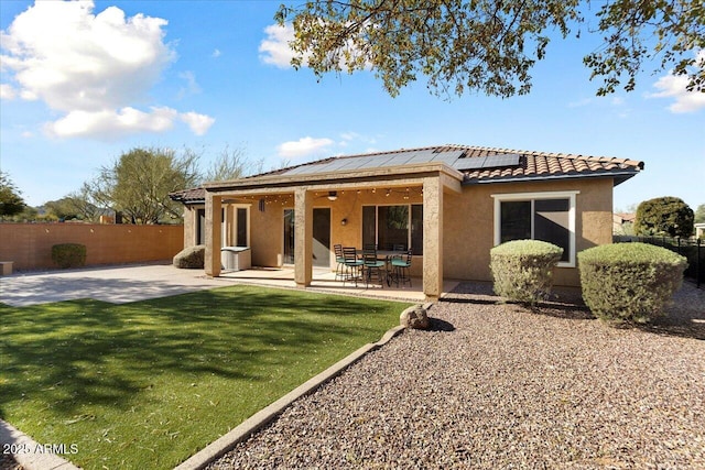 rear view of house with solar panels, a patio, and a lawn