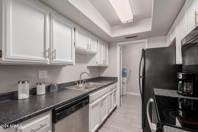 kitchen featuring a tray ceiling, dishwasher, white cabinets, and sink