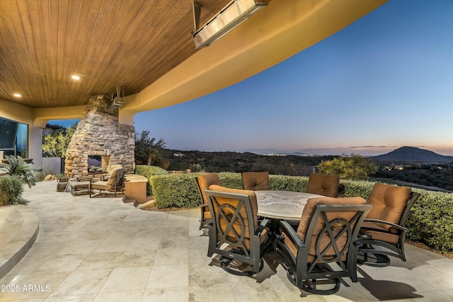 patio terrace at dusk featuring a mountain view and an outdoor stone fireplace