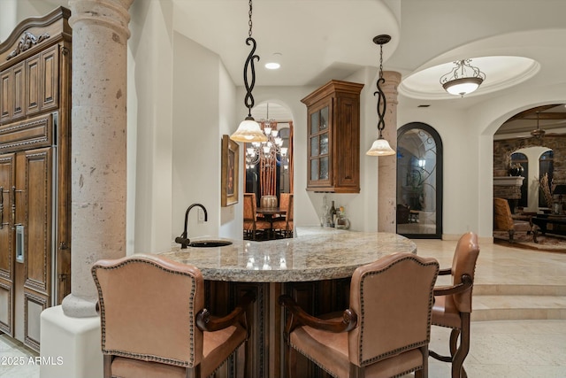 bar featuring light stone countertops, ornate columns, sink, hanging light fixtures, and ornamental molding