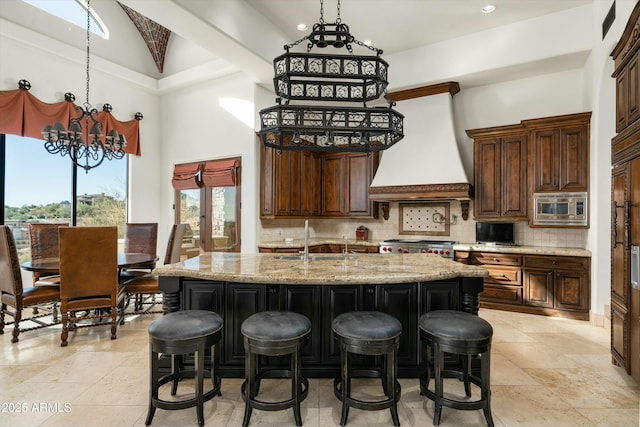 kitchen with stainless steel microwave, custom exhaust hood, a kitchen island with sink, and sink