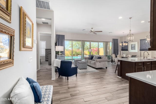 living room with sink, light wood-type flooring, and ceiling fan with notable chandelier