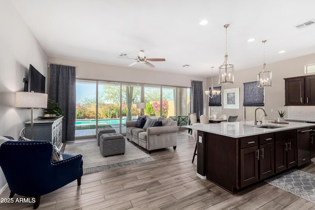 kitchen with hanging light fixtures, sink, a center island with sink, ceiling fan, and dark brown cabinetry