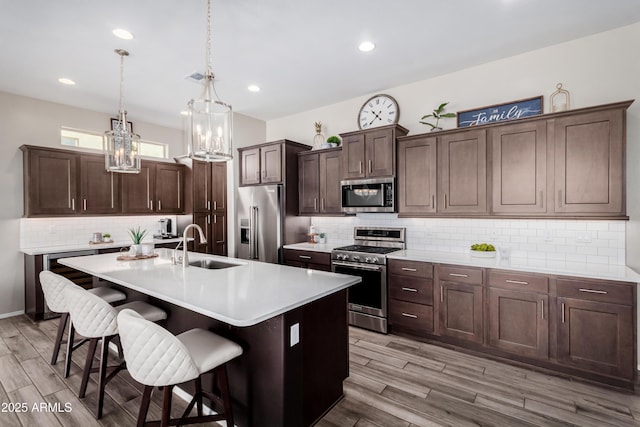 kitchen featuring a center island with sink, appliances with stainless steel finishes, light wood-type flooring, and dark brown cabinets