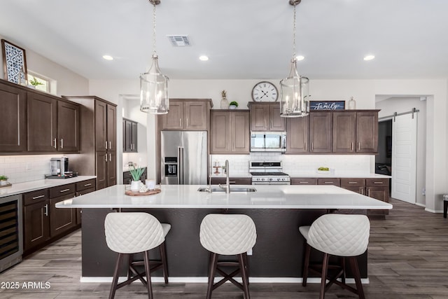 kitchen with sink, an island with sink, dark brown cabinets, a barn door, and high quality appliances