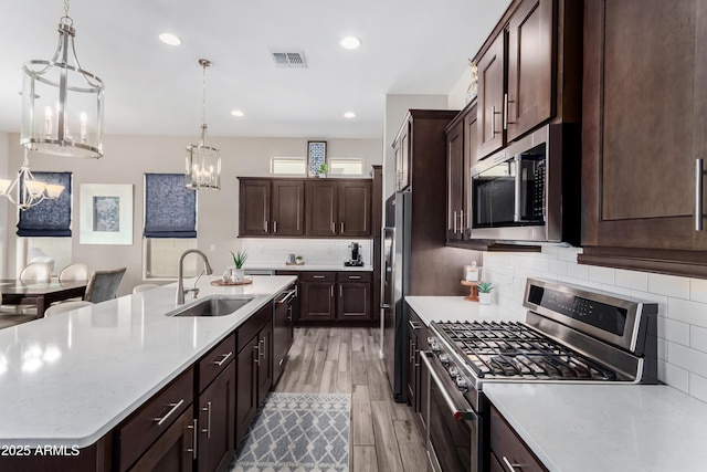 kitchen featuring a center island with sink, appliances with stainless steel finishes, hanging light fixtures, light hardwood / wood-style floors, and sink