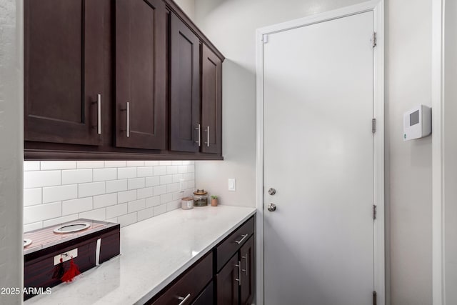 kitchen with backsplash, light stone countertops, and dark brown cabinetry