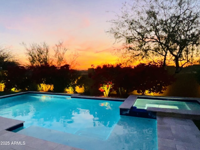 pool at dusk featuring an in ground hot tub