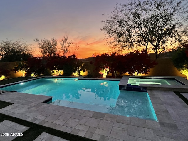 pool at dusk featuring a patio area and an in ground hot tub