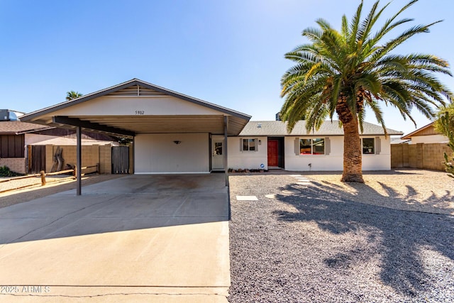 single story home with a carport, concrete driveway, and fence