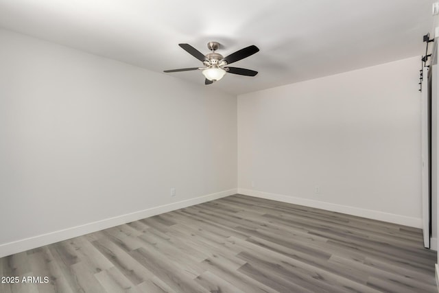 spare room with ceiling fan, a barn door, wood finished floors, and baseboards