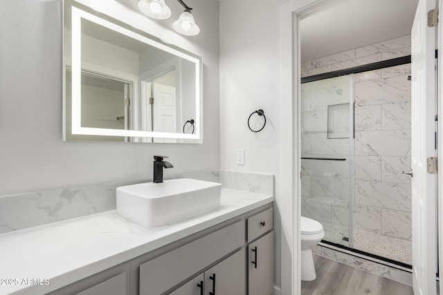 bathroom with toilet, a marble finish shower, wood finished floors, and vanity