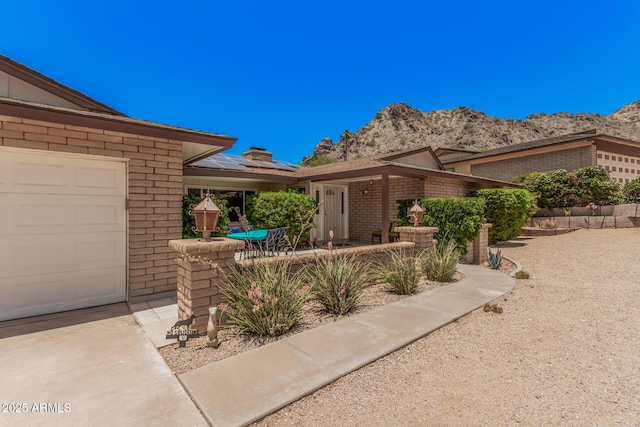 6802 N 26th St, Phoenix, AZ 85016 - view of front facade with roof mounted solar panels, brick siding, a mountain view, a garage, and a chimney