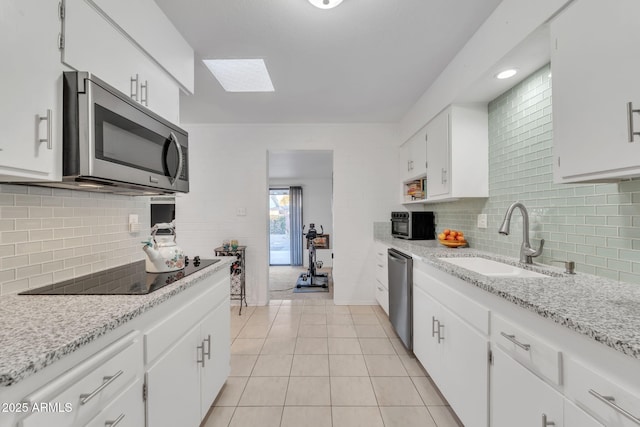 kitchen featuring light tile patterned floors, a skylight, appliances with stainless steel finishes, white cabinets, and sink