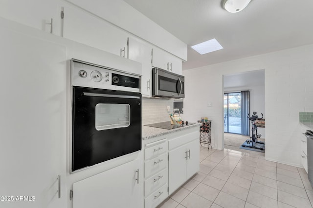 kitchen with black appliances, decorative backsplash, light tile patterned flooring, white cabinetry, and a skylight