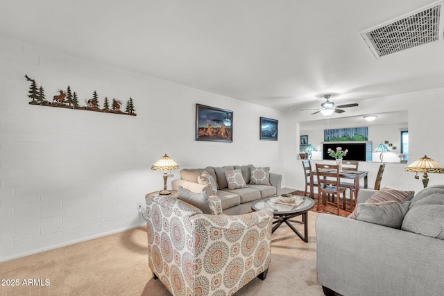 carpeted living room featuring ceiling fan and brick wall