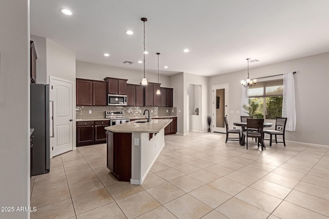 kitchen with pendant lighting, an inviting chandelier, a center island with sink, sink, and appliances with stainless steel finishes