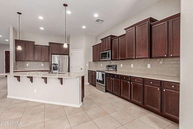 kitchen featuring a kitchen bar, stainless steel appliances, a kitchen island with sink, decorative light fixtures, and light tile patterned flooring