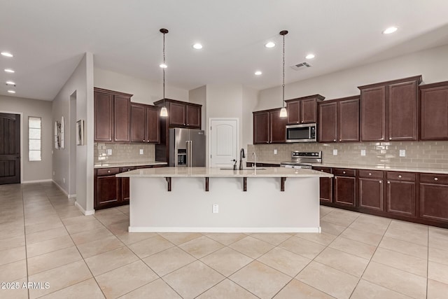 kitchen with a breakfast bar, stainless steel appliances, a kitchen island with sink, sink, and pendant lighting