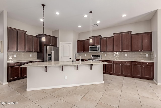 kitchen featuring a breakfast bar area, a center island with sink, decorative light fixtures, and appliances with stainless steel finishes