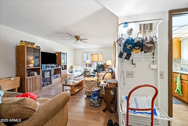 living area with a ceiling fan, light wood-type flooring, and a textured ceiling