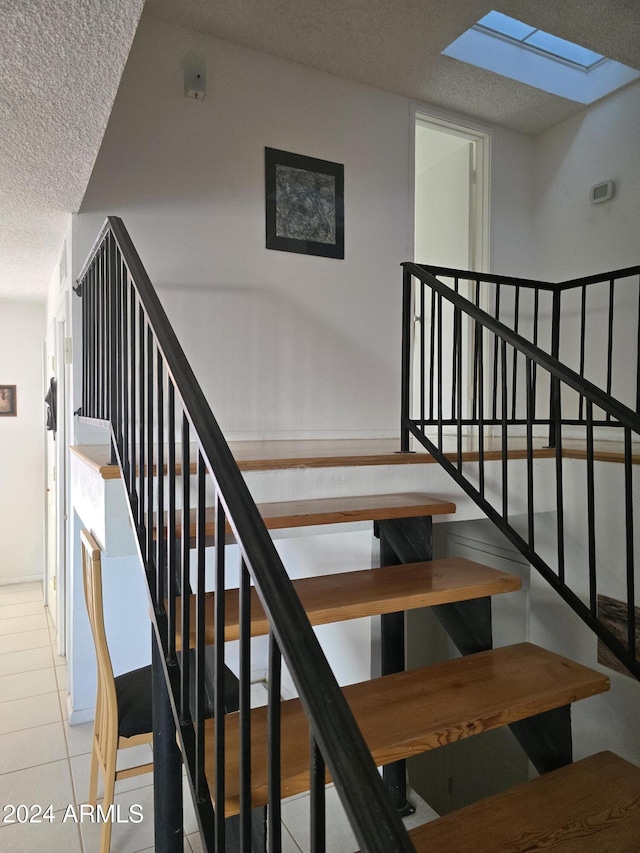 staircase featuring tile patterned floors, a textured ceiling, and a skylight