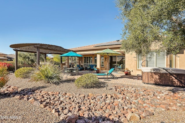 back of property featuring a patio area, a hot tub, and a pergola